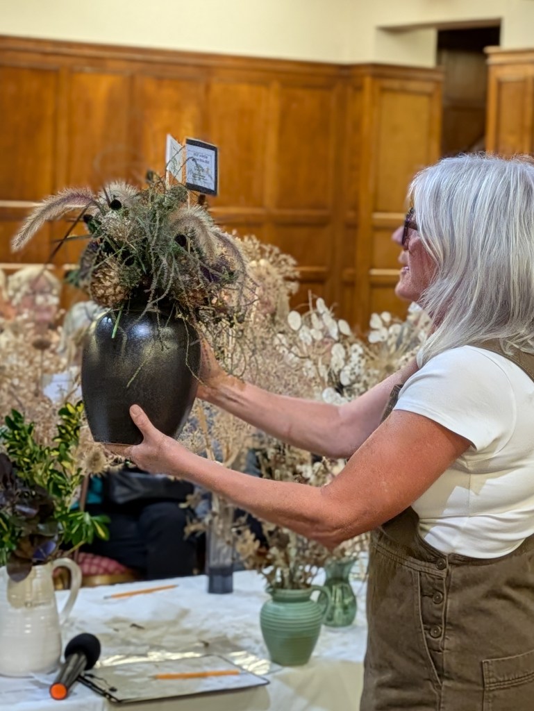 Judge Susan Urpeth commending Jayne's ornamental seedhead display for Class 6 (and Best in Show) CABAHS Autumn Show 2026